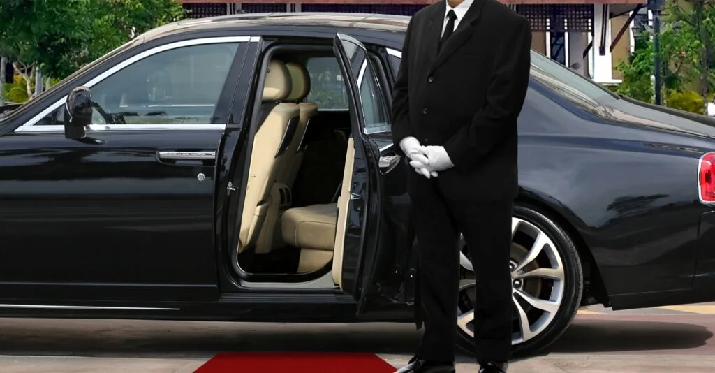 Chauffeur in Anzug und Handschuhen öffnet die Tür einer Limousine